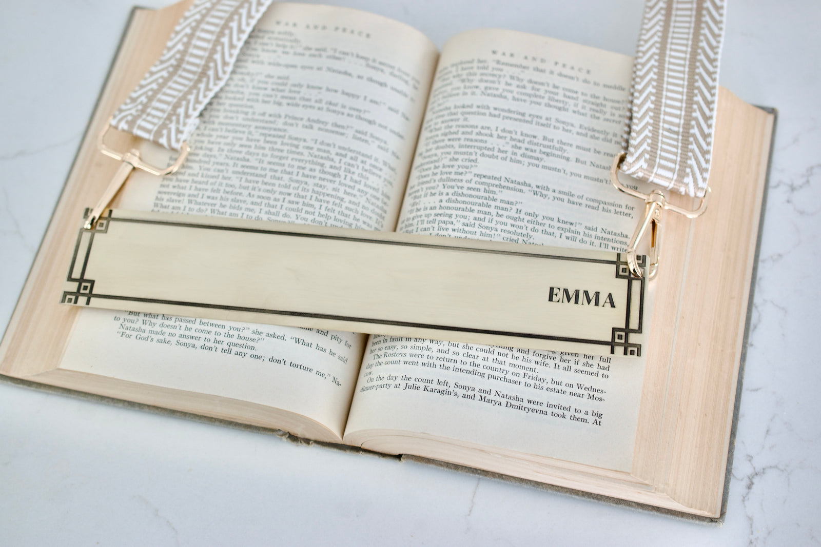 Open book with an engraved brass bookmark labeled 'Emma' attached to straps for book carrying