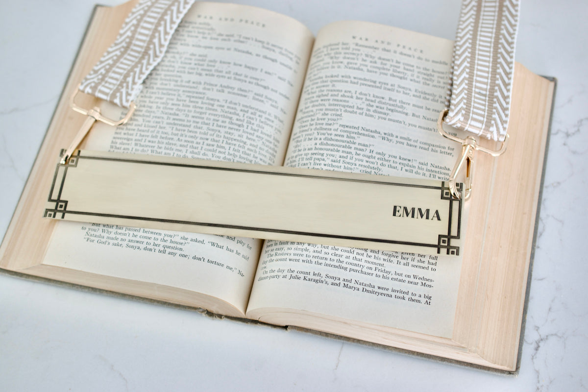Open book with an engraved brass bookmark labeled 'Emma' attached to straps for book carrying